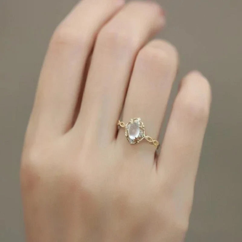 Gold-tone floral ring with a pale oval center worn on a hand.