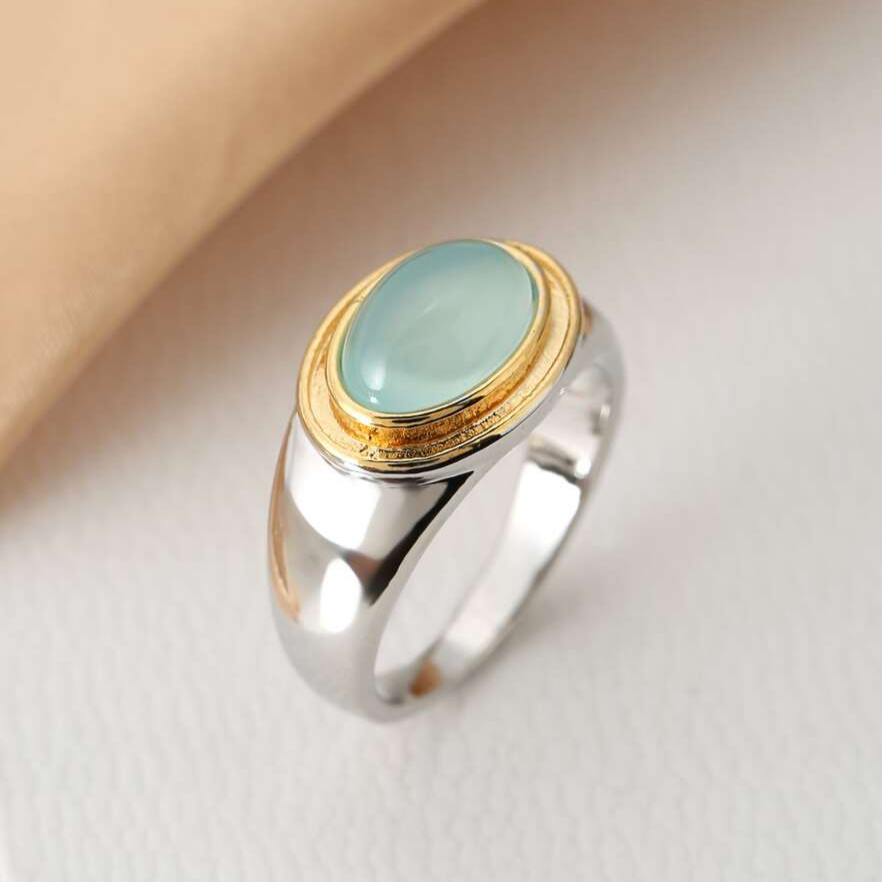 Ring with a pale green oval cabochon, textured gold-tone border, and broad silver-tone band.