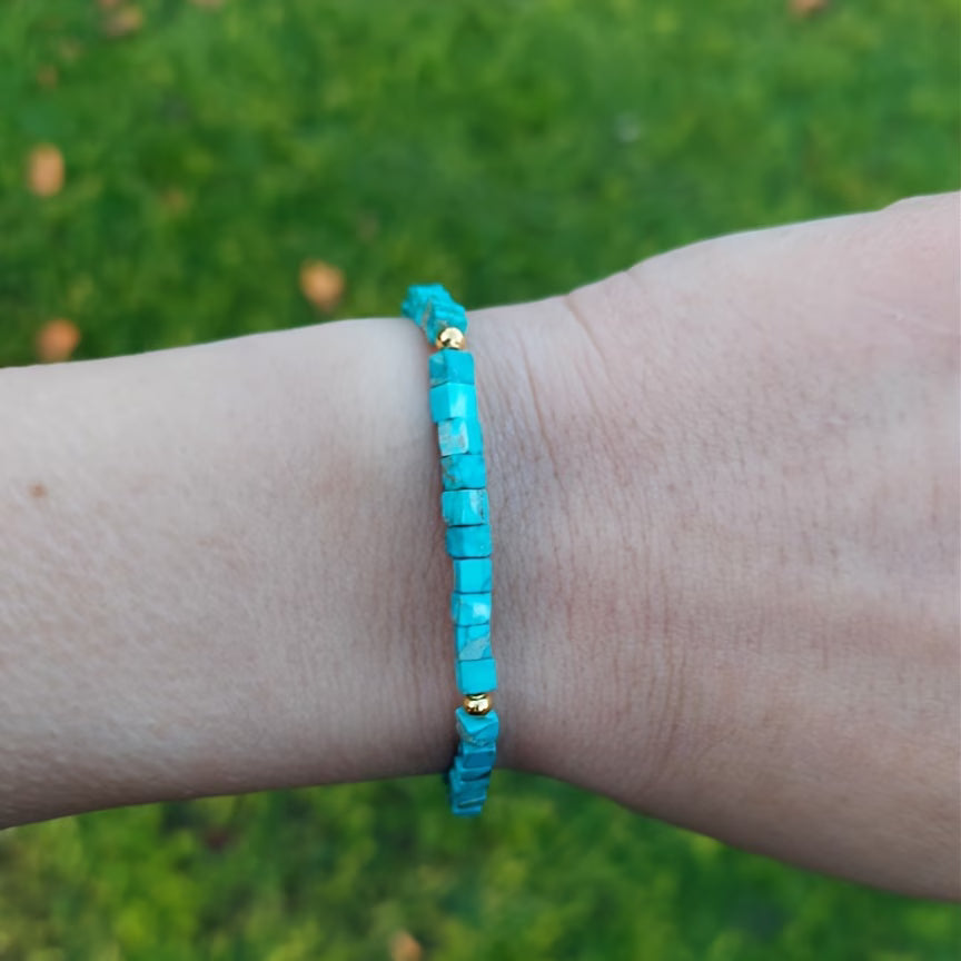 Turquoise-colored square bead bracelet on adjustable tan cord worn on the wrist.
