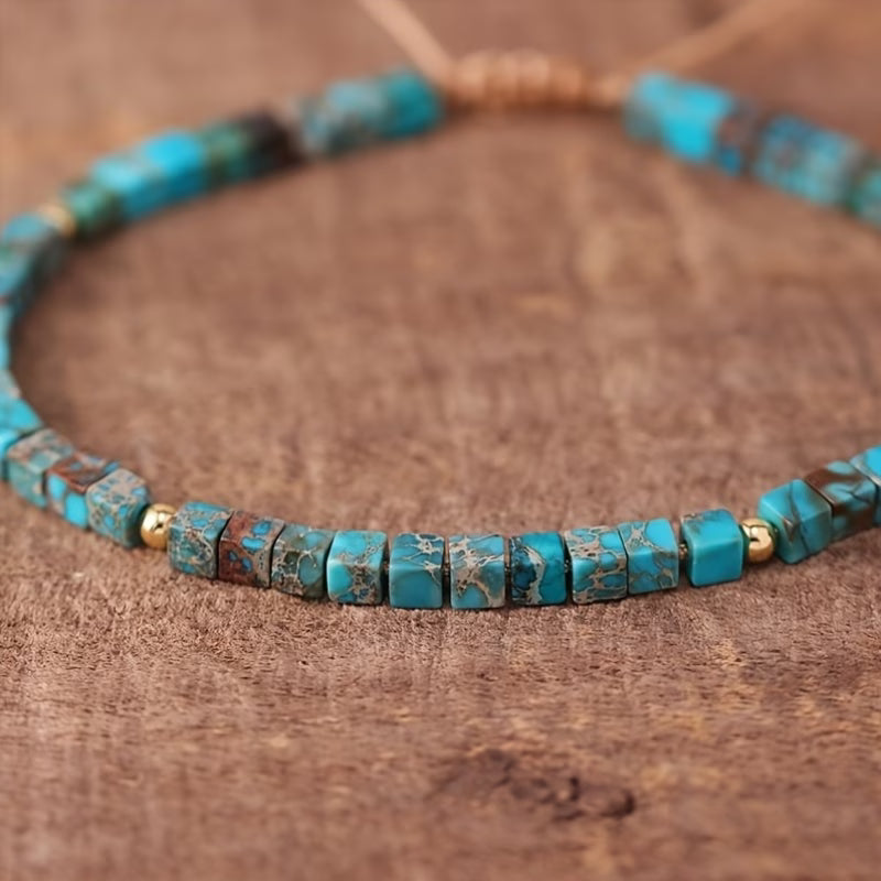 Turquoise-colored square bead bracelet with dark markings, small gold-tone spacers, and an adjustable tan cord.