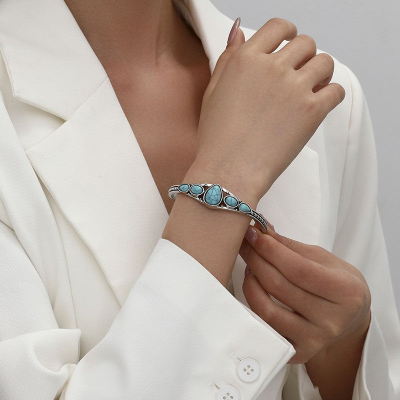 Model wearing a silver-tone open cuff with turquoise-colored teardrop and oval accents.