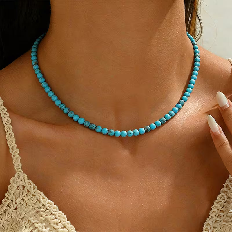 A person wearing a single strand necklace of small round turquoise-colored beads with dark markings.