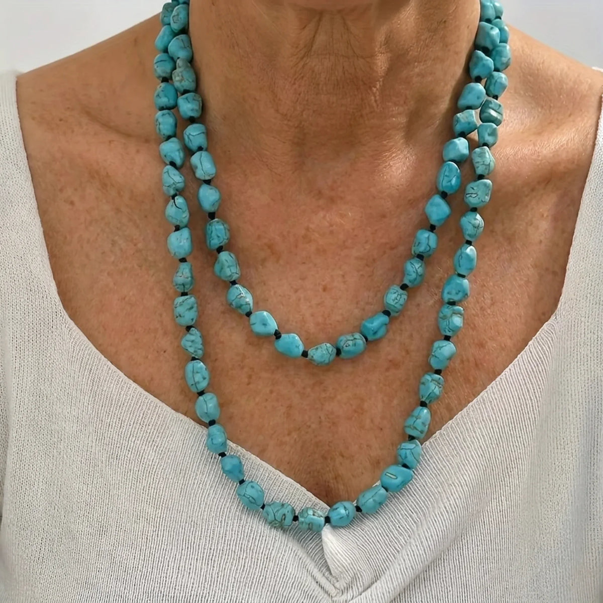 A person wearing two staggered strands of irregular turquoise-colored beads with dark webbed markings.
