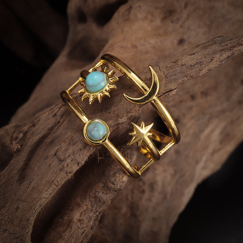 Gold-tone open multi-band ring with sun, crescent moon, star, and two pale-blue round accents.