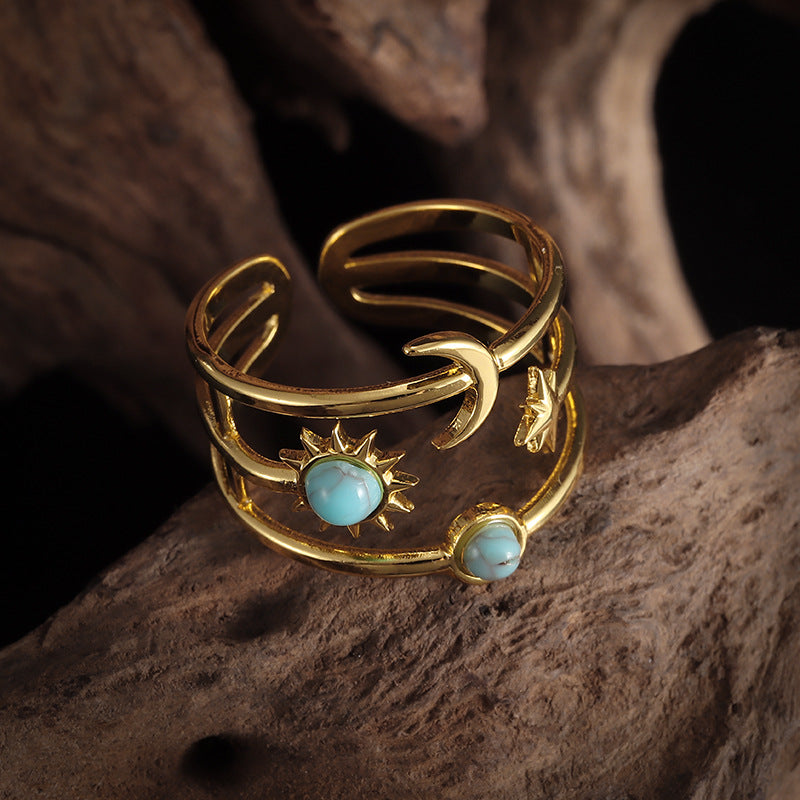 Gold-tone open multi-band ring with sun, crescent moon, star, and two pale-blue round accents.