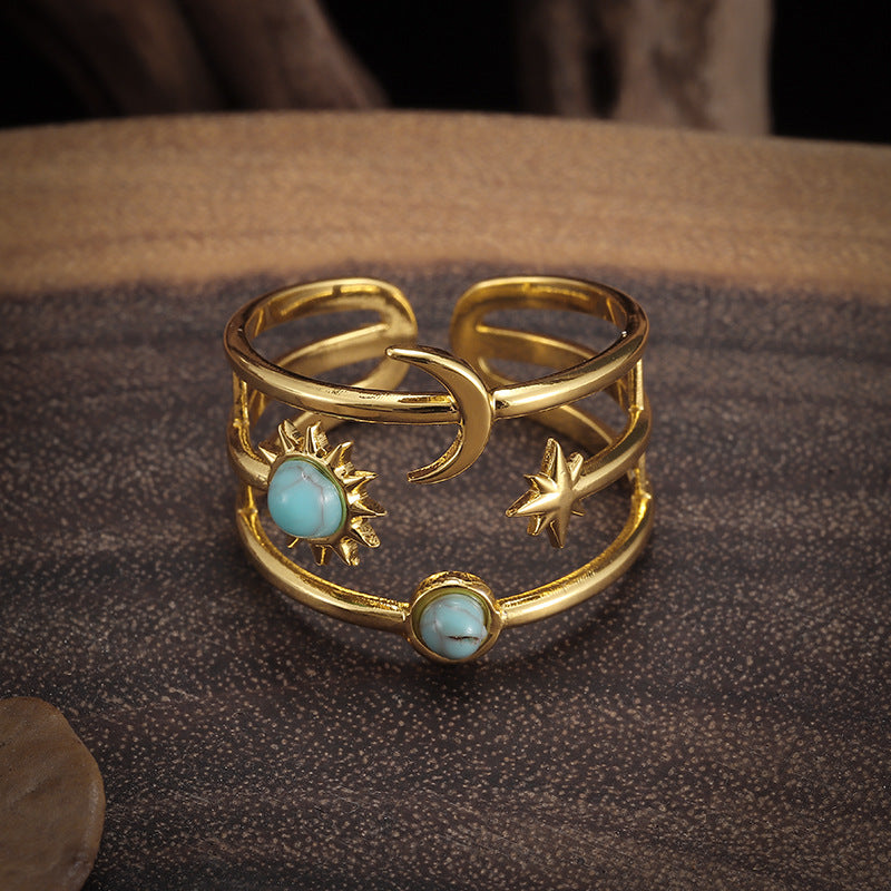 Gold-tone open multi-band ring with sun, crescent moon, star, and two pale-blue round accents.